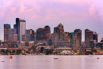 Modern buildings by river against sky during sunset