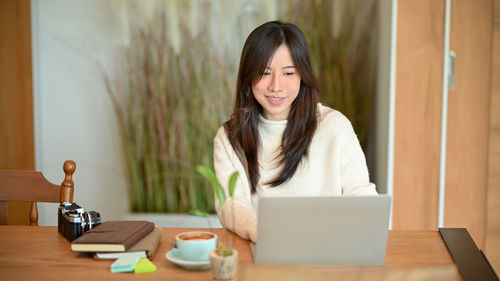 Young woman using mobile phone while sitting on table