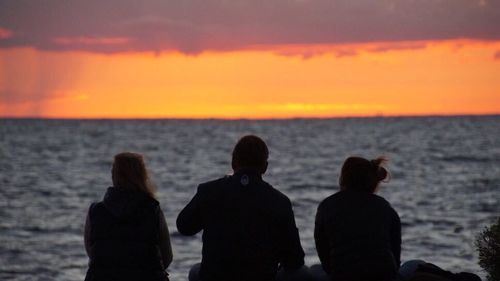 Silhouette of people looking at sea during sunset