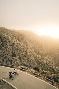 High angle view of male and female friends cycling on road with mountains in background at sunset