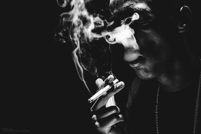 Close-up of man holding cigarette against black background