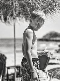 Side view of shirtless young woman standing at beach