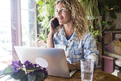 Young woman using mobile phone while sitting on table