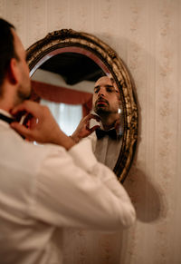 Mirror portrait of handsome young man putting on a bow tie.