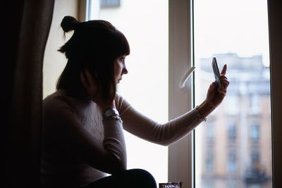 Woman taking selfie while sitting on window sill