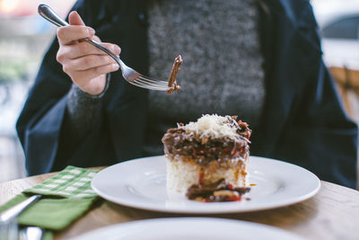Midsection of woman eating dessert at table