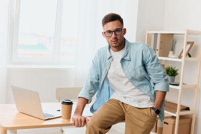 Portrait of young man using laptop while standing in office