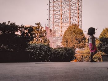 Side view of girl standing by trees against sky