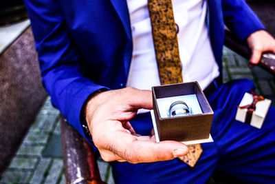 Midsection of bridegroom holding wedding rings while sitting outdoors