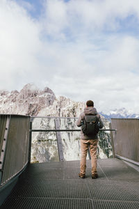 Rear view of man standing on railing against sky