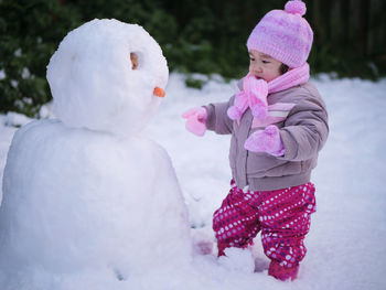 Cute toddler girl standing by snowman during winter