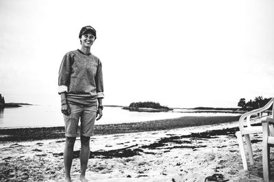 Portrait of young woman standing on beach against clear sky