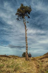 Man standing by tree on field against cloudy sky