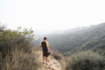 Rear view of man standing on mountain against sky