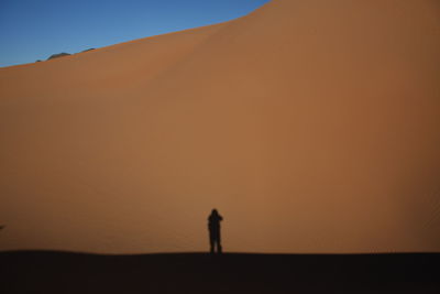 Silhouette person standing on desert against sky during sunset