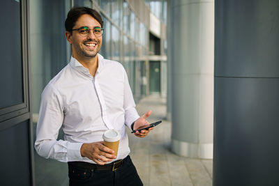 Portrait of young smilling business man standing near office building