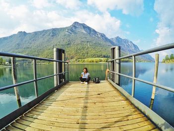 Smiling woman sitting on pier over lake against mountains