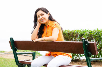 Smiling young woman sitting on chair against sky