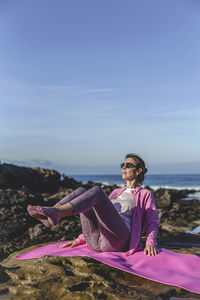 Woman exercising at sea against sky