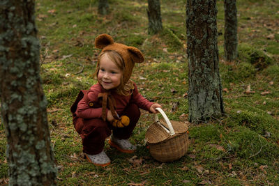 Toddler baby girl in bear bonnet sitting in the woods