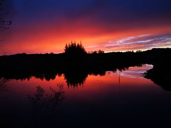 Silhouette trees by lake against romantic sky at sunset