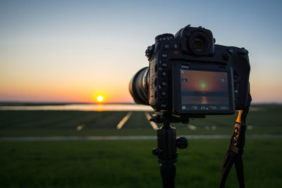 Close-up of camera on field against sky during sunset