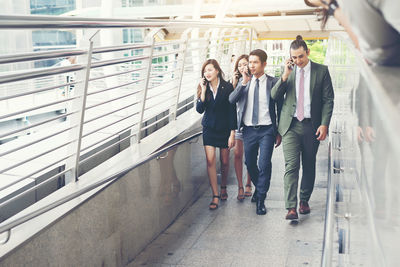 Colleagues using phones while walking on elevated walkway 