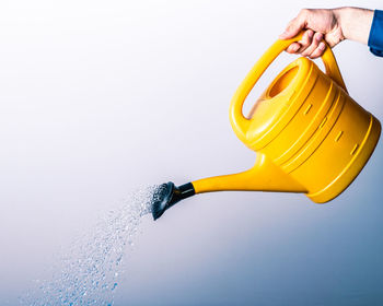 Close-up of hand holding yellow umbrella against white background