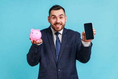 Man with piggy bank and smart phone against blue background