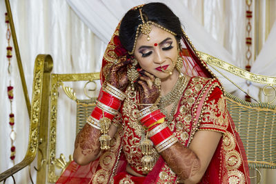 Bride in sari wearing jewelry while sitting on porch swing