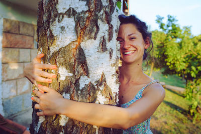 Portrait of smiling young woman holding tree trunk