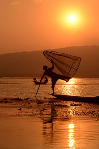 Fisherman fishing in lake with conical fishing nets during sunset