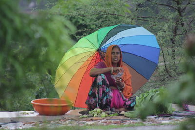 Portrait of woman selling vegetables while sitting under umbrella