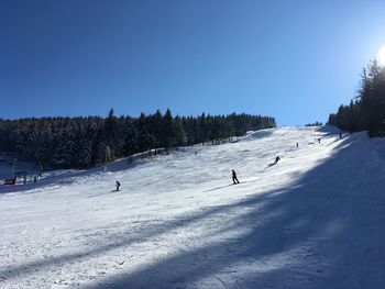 People skiing on snow covered landscape against clear sky