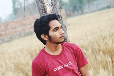 Young man looking away standing by tree trunk