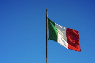 Low angle view of flags against clear blue sky