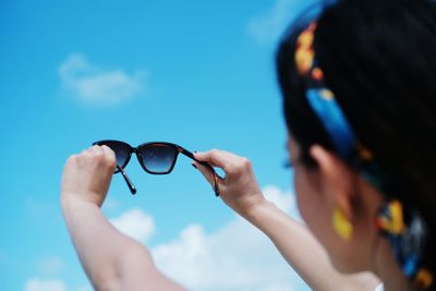 Midsection of woman wearing sunglasses against blue sky