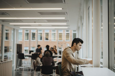 Side view of young student studying at table in university