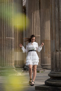 Full length of young woman standing against columns