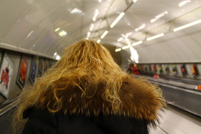 Rear view of woman wearing warm clothing while standing at illuminated subway station