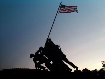 Silhouette statue with american flag against clear sky during sunset