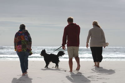 Rear view of people walking on beach against sky