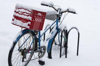 Snow covered blue bicycle with red milk crate basket