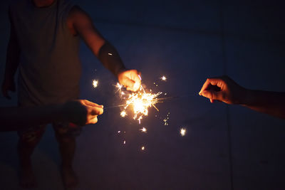 Cropped hands of people holding sparklers at night