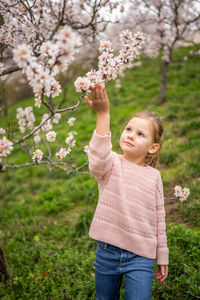 Portrait of young woman with arms outstretched standing against tree