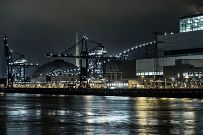 Illuminated buildings by river against sky at night