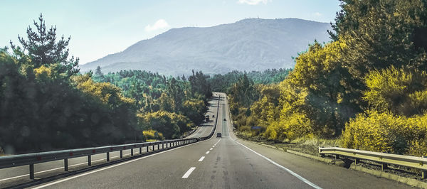 Road amidst trees and mountains against sky