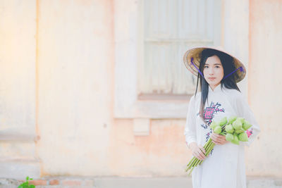 Portrait of young woman holding buds against building