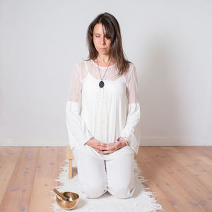 Adult caucasian woman dressed in white during a meditation sesion. metal singing bowl next to her.