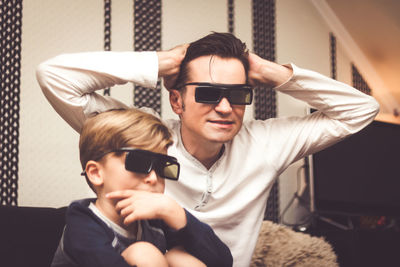 Father with son watching tv while sitting against wall at home